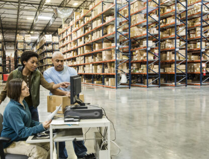 Warehouse workers checking inventory on a computer in a large distrubiton warehouse.