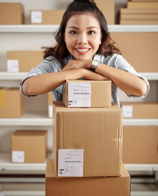 Portrait of Asian young office worker standing with heap of cardboard boxes preparing for delivery